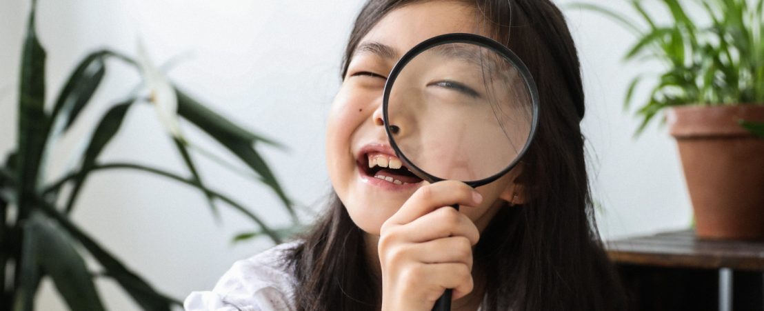 Una niña con hipermetropía infantil  sujeta una lupa frente a su ojo